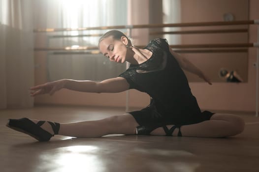 Woman in pointe shoes sits on the floor and does ballet warm-up