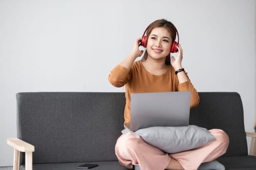 Young woman sitting on a sofa with a laptop and headphones, enjoying a relaxing moment at home.