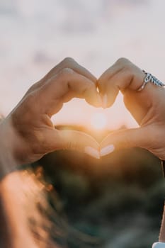 A woman's hand is holding a heart shape, with the sun shining on it. Concept of love and warmth, as the sun symbolizes happiness and positivity. The heart shape represents the bond between two people