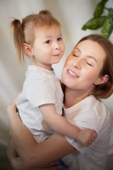 Happy loving family. Mother and daughter child girl playing and hugging in living room with wicker chair