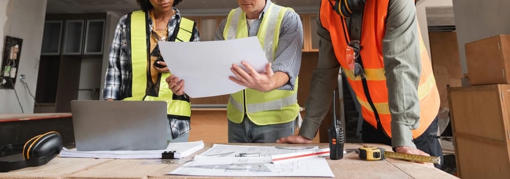 Engineering team in safety vests reviewing blueprints and using digital tools for construction planning in a modern workspace.