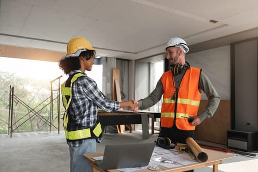 Engineering team planning construction work, shaking hands in agreement on a building site. Collaboration and teamwork in modern architecture projects.