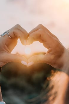 A woman's hand is holding a heart shape, with the sun shining on it. Concept of love and warmth, as the sun symbolizes happiness and positivity. The heart shape represents the bond between two people