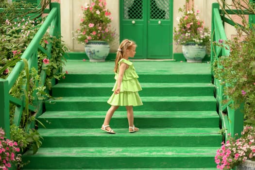 A girl in a green dress in the gardens of Claude Monet in Giverny. Facade and stairs of the Monet's house