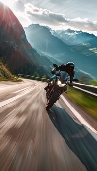 A man speeds on a motorcycle along a winding mountain road. The scenic background of mountains and forests is blurred, emphasizing the motorcycles speed.