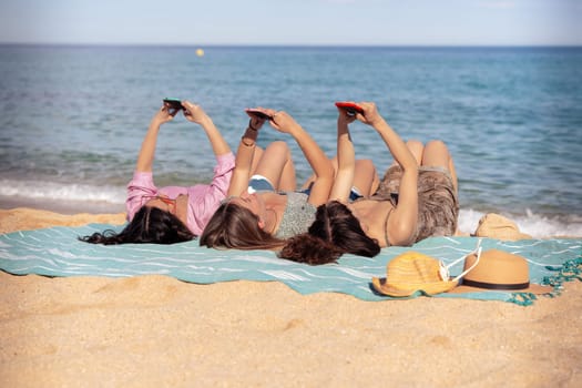 Three young women using apps on their cell phones on the beach