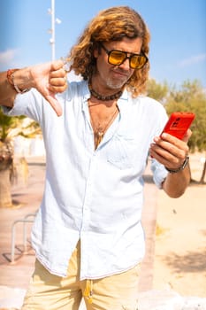Caucasian man wearing sunglasses feeling serious showing his finger down in disapproval outdoors.