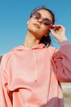 Stylish woman in pink sweatshirt and sunglasses posing confidently in the desert landscape