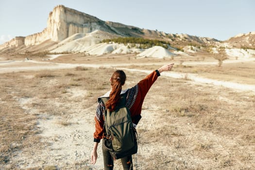 female explorer in desert with backpack and outstretched arms in awe of vast landscape