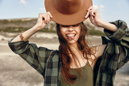 Stylish woman in plaid shirt and hat standing confidently in a rustic field