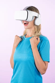 Caucasian happy girl wearing VR glasses and making winner gesture. Skilled woman celebrate while winning game by using VR headsets and standing at pink background. Technology innovation. Contraption.