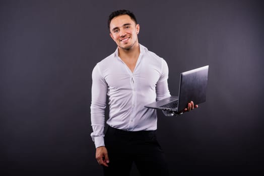 Image of a young cheerful businessman holding and using laptop isolated over dark background