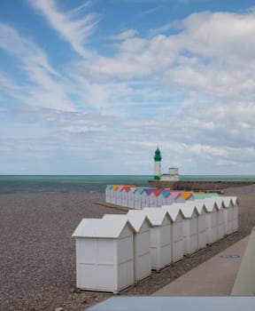wooden beach houses with different colored roofs on the beach of le treport in France Normandy with the lighthouse at the background