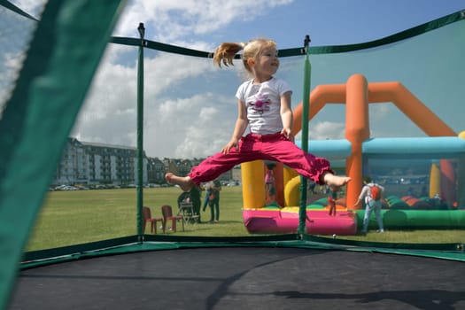 Girl in fuchsia pants jumping on a trampoline at a summer