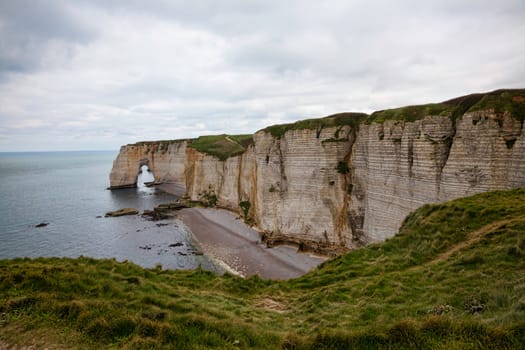 Landscape photo of tall, steep limestone cliffs by the ocean with one with a hole in it creating an arch