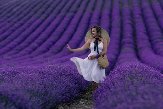 A woman is standing in a field of purple flowers. She is wearing a white dress and a straw hat