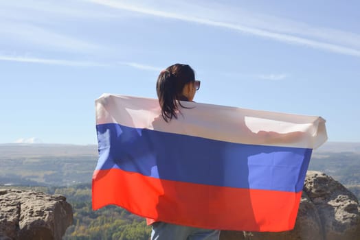 The Russian flag is on the shoulders of a girl standing against the backdrop of the Caucasus mountains. Unity Day in Russia