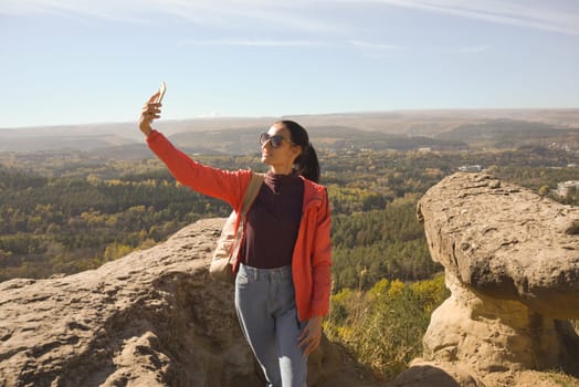 Young beautiful woman traveler taking selfie portrait on mountain top - Happy smiling girl using smartphone - Hiking and climbing rock.