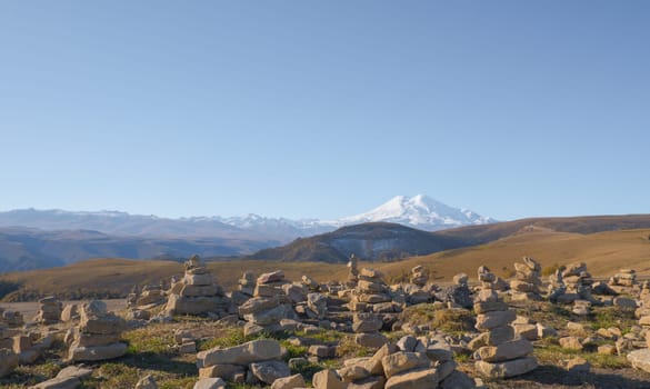 Mountain Elbrus. Autumn Elbrus. Autumn in the Caucasus mountains. Gilli-Suu district. Landscape of snow-capped mountains through stone pyramids. Snowy peaks. Panorama of Elbrus