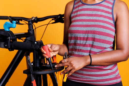 Black individual selecting specialized work tools for yearly bicycle maintenance. Detailed view showing female african american arm organising a variety of professional tools for fixing damaged bike.