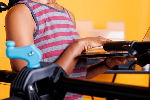 Close-up of african american person holding wireless computer for bicycle maintenance. Detailed image shows healthy black woman grasping laptop next to bike frame clamped to a repair-stand.