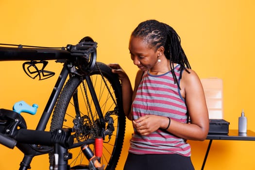 Against an isolated background, sports-loving lady performs yearly maintenance and adjustment of bicycle tyre. Youthful african american woman inspects her bike wheel for leisure cycling.