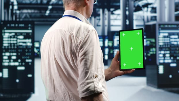 Technician in high tech data center using green screen tablet to monitor energy efficient servers using renewable sources employed to minimize consumption and reduce overall facility carbon footprint