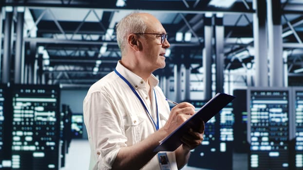 Elderly engineer looking around high tech data center, using clipboard to crosscheck disaster recovery plan and assess server components in need of replacement, preventing failures