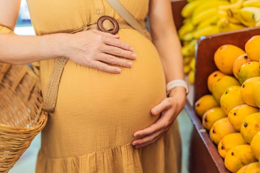 In a grocery store, a pregnant woman stands by a fruit stand, surrounded by various natural foods. She is in a public space where the local market offers whole foods for trade Pregnant woman buying organic vegetables and fruits at Mexican style farmers market