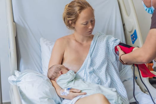 A woman in a hospital breastfeeds her baby while a nurse checks the mother s health. The nurturing moment showcases the bond between mother and child, while the attentive nurse ensures the mother's well-being, creating a supportive environment for both.