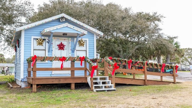 Discover a picturesque small blue cottage adorned with a welcoming wreath, twinkling Christmas lights, and surrounded by two lovely palm trees in the yard, creating a cozy holiday retreat.