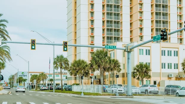 The image shows a street with palm trees on the sides and a tall apartment building in the background. The sky is cloudy and the light is coming from the right side of the image.