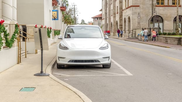 A white Tesla Model 3 electric car parked in the city surrounded by buildings and trees. New, clean, and in a parking spot. Low angle, well-lit, suitable for stock agencies.