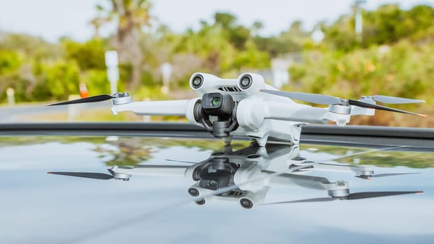 A sleek white quadcopter drone with four propellers is perched on the roof of a shiny black car against a blurred urban background, showcasing technology and innovation.