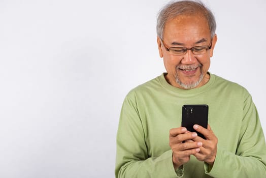 Portrait smiling Asian older man smiling holding a cell phone studio shot isolated on white background. elderly typing message on mobile phone in hand. Concept of connection and communication