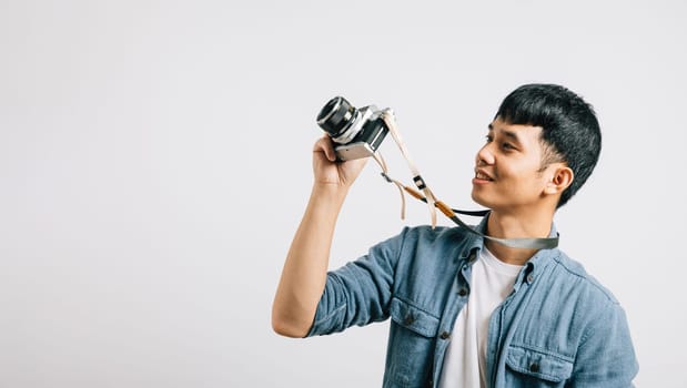 A dashing young man enjoys a photography moment with a vintage camera. Studio shot isolated on white background. The picture is a snapshot of pure paparazzi excitement