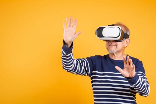Portrait Asian smiling old man touching at something in a virtual reality glasses headset studio shot isolated yellow background, Excited happy senior man pensioner using VR play simulation game