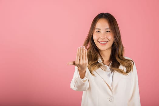 Happy Asian portrait beautiful cute young woman teen smile positive friendly making gesture hand inviting to come here with hand look to camera studio shot isolated on pink background with copy space
