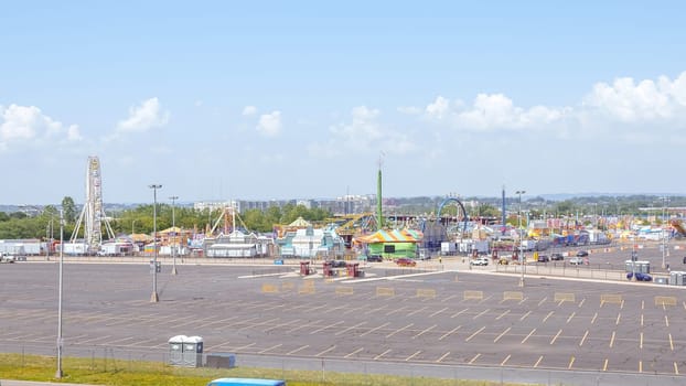 An amusement park with Ferris wheels and roller coasters under a blue sky with white clouds. The rides are colorful and bright. There are a lot of people in the park having fun.