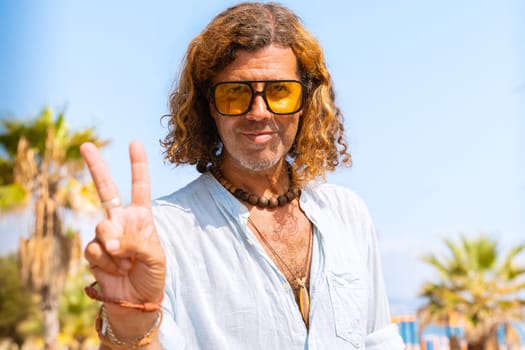 Caucasian man wearing sunglasses feeling happy showing peace symbol outdoors.