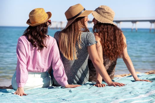 Group of smiling multiethnic women in hats and sunglasses enjoying vacation looking out to sea. Beautiful and cheerful girls of Generation Z