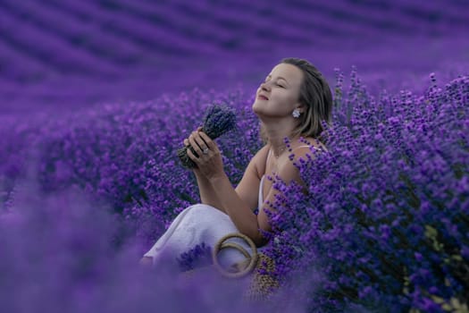 A woman sits in a field of lavender flowers, holding a bunch of lavender in her hand. She is enjoying the scent and the peaceful atmosphere of the field