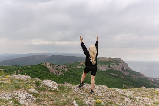 A woman is standing on a mountain top, looking out over the ocean. She is wearing a black shirt and shorts and she is in a joyful, uplifting mood