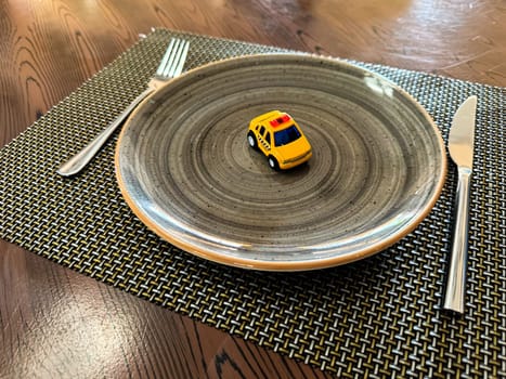 Miniature taxi toy on ceramic plate with cutlery. Concept of calling taxi after end of banquet or celebration. Design of taxi advertising, culinary presentations and unusual concepts. High quality