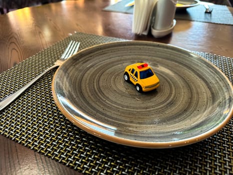 Miniature taxi toy on ceramic plate with cutlery. Concept of calling taxi after end of banquet or celebration. Design of taxi advertising, culinary presentations and unusual concepts. High quality