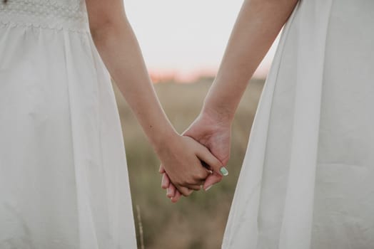 two girls holding hands together in the summer outdoors. Unity and family happiness. Added a small grain simulation of film photography