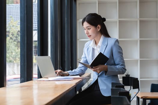 Young accountant working diligently in a modern office, using a laptop and notebook, showcasing professionalism and focus.