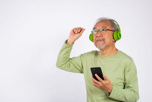 Portrait Asian smiling old man headphones is holding smartphone listen music in headphones and dancing studio shot isolated on white background, Funny senior, enjoying his music
