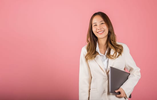 Business woman smiling confident smiling holding closed laptop, Portrait excited happy Asian young female person hugging close cover computer device studio shot isolated on pink background