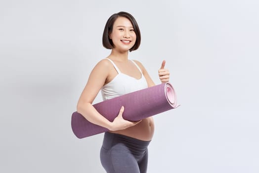 Portrait of a young pregnant woman holding a yoga mat in the studio on a white background